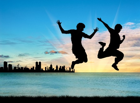 Concept of gay people. Silhouette of two happy gays jump on the background of sea sunset and cityの写真素材