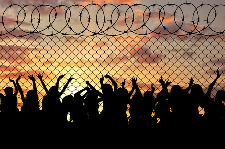 Concept of the refugees. Silhouette of a crowd of refugees at the border at sunsetの写真素材