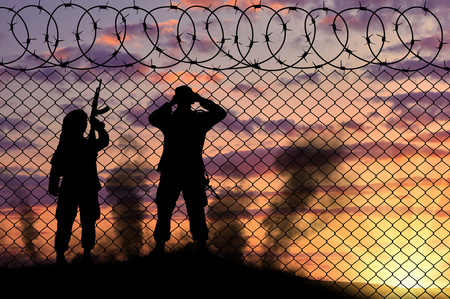 Concept of terrorism. Silhouette scouts terrorists near the border fence at sunset in smokeの写真素材