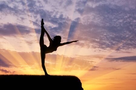 Concept of meditation and relaxation. Silhouette of a girl practicing yoga exercise on the sunset backgroundの写真素材