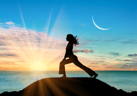Concept of meditation and relaxation. Silhouette of a girl practicing yoga class on a background of sea sunsetの写真素材