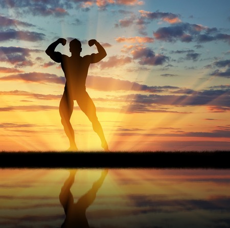 Concept of beauty and sports. Silhouette of bodybuilder posing at sunset and its reflection in waterの写真素材