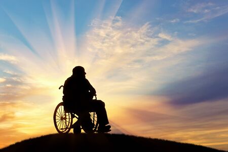 Concept of disability and old age. Silhouette of disabled person in a wheelchair on the sunset backgroundの写真素材
