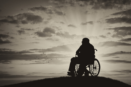 Concept of disability and old age. Silhouette of disabled person in a wheelchair on the sunset backgroundの写真素材