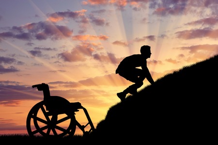 Concept of disability and self-motivated. Silhouette of disabled person to climb the hill at sunsetの写真素材