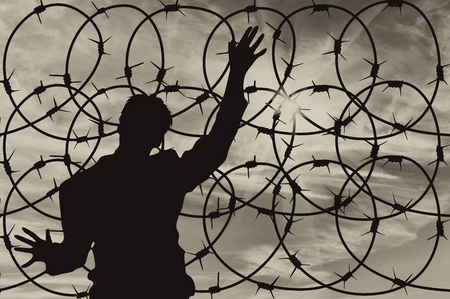Concept of security. Silhouette of refugee men and metal fence with barbed wire on the background of the beautiful skyの写真素材
