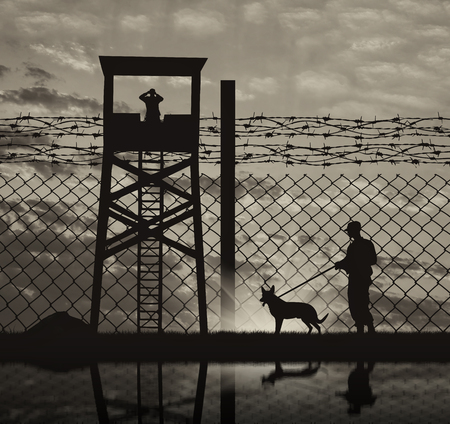 Concept of security. Silhouette of a lookout tower and a guard with a dog on the background of the fence with barbed wire and reflectionの写真素材