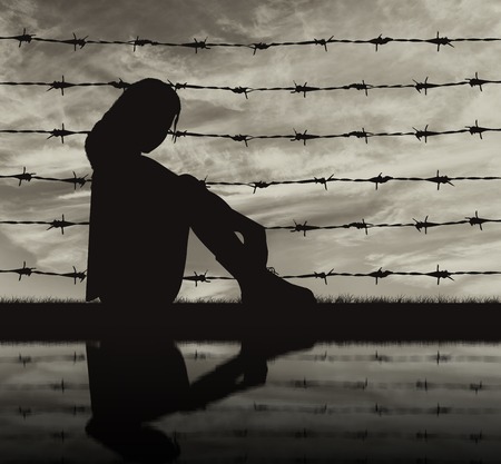 Concept of refugee. Silhouette Despair refugee woman near the fence of barbed wire and reflectionの写真素材