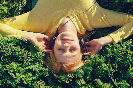 Concept of music. Young woman with headphones listening to music on meadowの写真素材