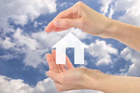 Real estate concept. Icon of an apartment house in human hands against the skyの写真素材