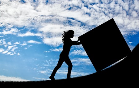 Silhouette of a strong woman pushing a cube to the top. Concept of effort and difficultiesの写真素材