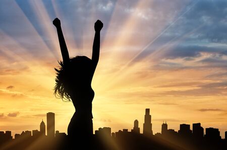 Silhouette of a happy woman on a background of the urban landscape at sunsetの写真素材