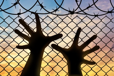 Refugees concept. Silhouette refugee hands near the barbed wire fenceの写真素材