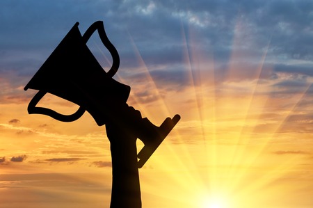 Champion and winning concept. Silhouette of a hand holding a championship trophy against the skyの写真素材