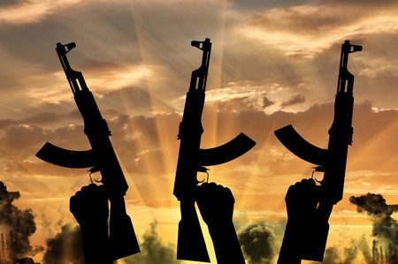 Terrorists concept. Weapons in the hands of terrorists, against the background of a sunset in the smokeの写真素材