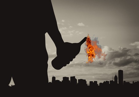 Terrorist concept. Silhouette of a terrorist holding a molotov cocktail on the background of the cityの写真素材