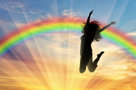 Rainbow and happiness. Happy woman jumping at sunset near the rainbowの写真素材