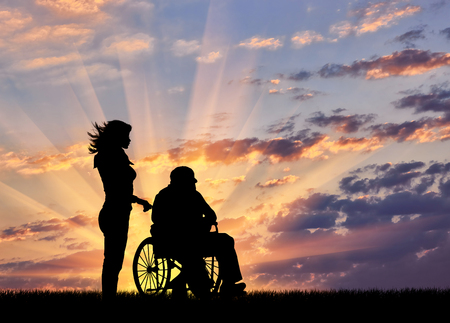Silhouette of a nurse caring for a disabled person in a wheelchair. Concept of caring for a disabled person and the house of agedの写真素材