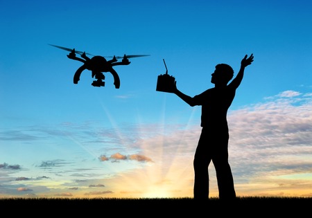 Silhouette of a flying drone, and a man with a remote control at sunset. Concept quadrocoptersの写真素材