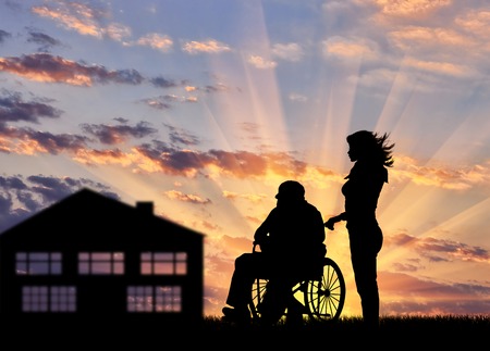 Silhouette of a nurse caring for a disabled person in a wheelchair. Concept of caring for a disabled person and the house of agedの写真素材