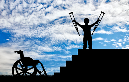 Happy disabled boy standing on sters with crutches in his hands and wheelchair day. Concept happy disabledの写真素材