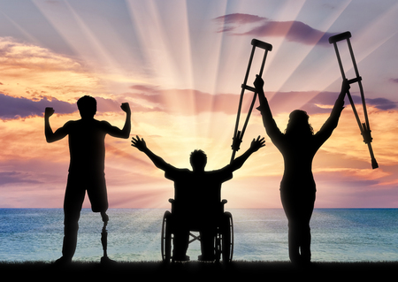 Three happy disabled with prosthesis and crutches and in wheelchair near sea. Concept happy disabledの写真素材
