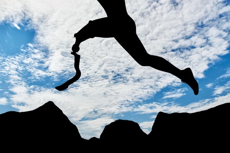 Disabled athlete with prosthetic leg jumping over rocks on background of sky. Concept disability and sportの写真素材