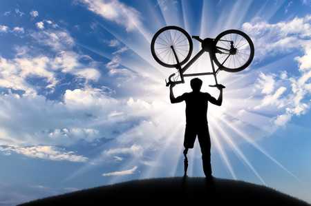 Disabled with prosthetic leg standing on hill and holding bicycle over his head day. Concept disabled and sportの写真素材