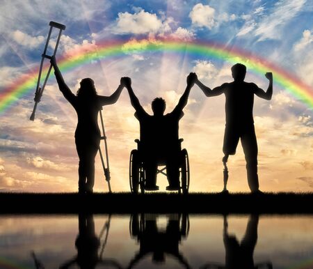 Invalids on crutches and in wheelchair and prosthesis in foot standing on rainbow background and holding hands. Concept happy disabledの写真素材