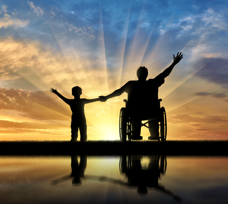 Happy disabled person in wheelchair hold son for hand and they happy and with their reflection in water on sunset. Concept happy disabled and familymilyの写真素材