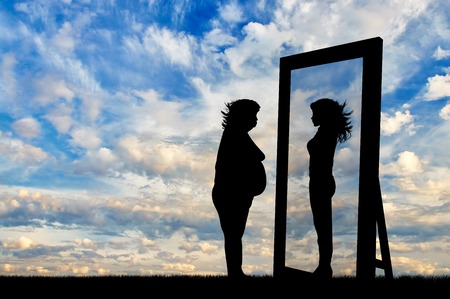 concept of fight against obesity and the desire to be slim. Silhouette thick and slender woman reflected in a mirrorの写真素材