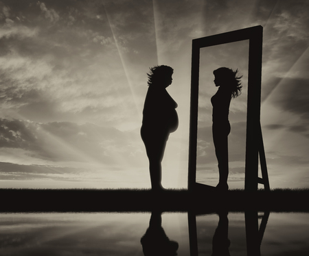 concept of fight against obesity and the desire to be slim. Silhouette thick and slender woman reflected in a mirrorの写真素材