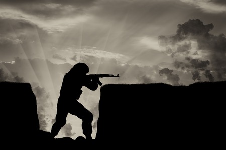 terrorist with a weapon in trenches against the sky in smoke. concept of conflict and warの写真素材