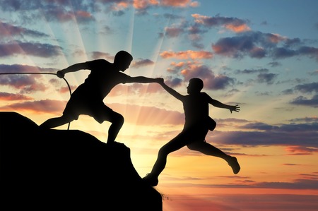 Mountaineer takes a helping hand to his partner. Teamwork and trust conceptの写真素材