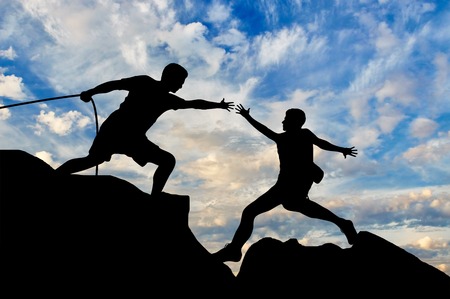 Mountaineer takes a helping hand to his partner. Teamwork and support conceptの写真素材