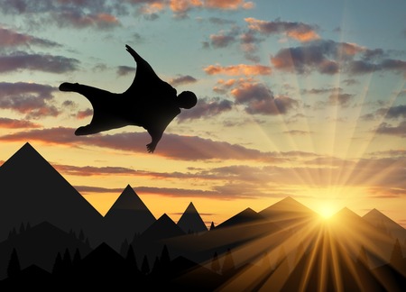 Wingsuit extreme sports. A man in a suit for wingsuit flying, mountains in background at sunsetの写真素材