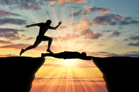 Man runs through a man lying on precipice. Concept of competitionの写真素材