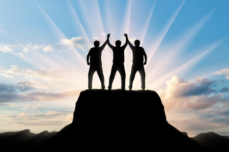 Silhouette of happy three climbers on the top of the mountain holding hands. Concept of teamworkの写真素材