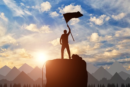 Silhouette of a climber on a mountain top with a flag in his hand. success conceptの写真素材