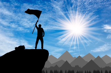 Silhouette of a climber on a mountain top with a flag in his hand. success conceptの写真素材