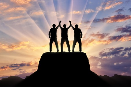 Silhouette of happy three climbers on the top of the mountain holding hands. Concept of teamworkの写真素材