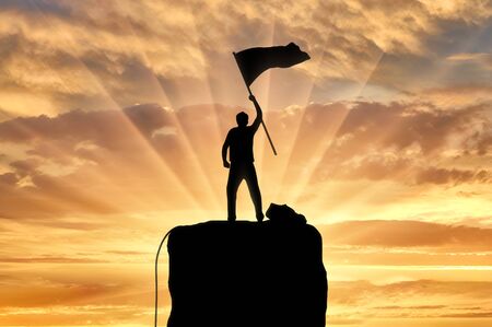 Silhouette of a climber on a mountain top with a flag in his hand. Concept of success and motivationの写真素材