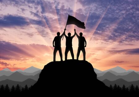 Silhouette of two climbers on a mountain top with a flag in his hand. Concept of a business teamの写真素材