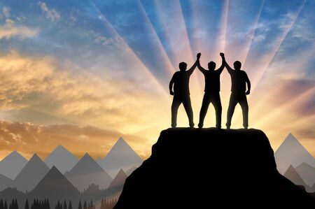 Silhouette of happy three climbers on the top of the mountain holding hands. Concept of teamworkの写真素材