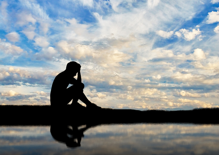 Child abuse and violence. Silhouette of a crying boy by the river against skyの写真素材