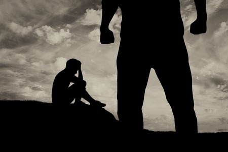 Child abuse and bullying in the family. Silhouette of a crying frightened boy and aggressive father with fistsの写真素材