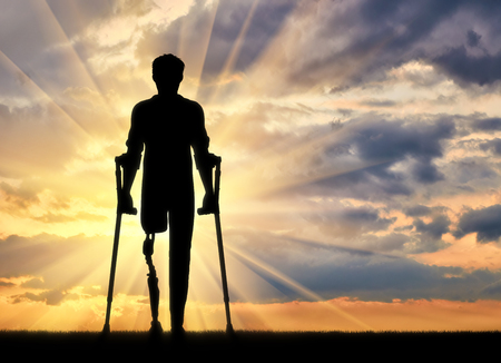 Disabled person with a prosthetic leg and crutches at sunsetの写真素材