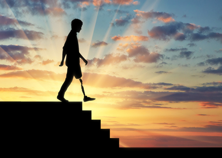 Disabled person with a prosthetic leg descends down the stairs at sunsetの写真素材