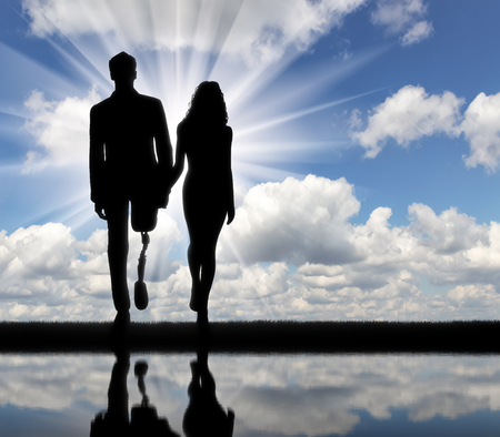 Disabled person with a prosthetic leg, walking with a woman holding hands, and theirs reflection in the riverの写真素材
