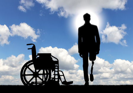 Disability and rehabilitation. Walking is a disabled man with a prosthetic leg and a wheelchair outdoorsの写真素材